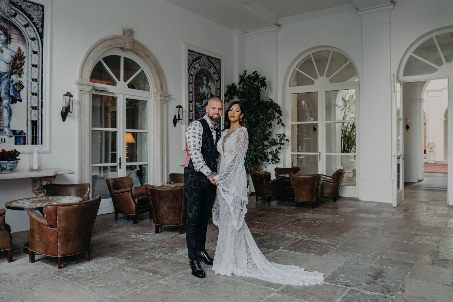 Elegant wedding portrait in a bright conservatory with arched windows and classic leather furniture.