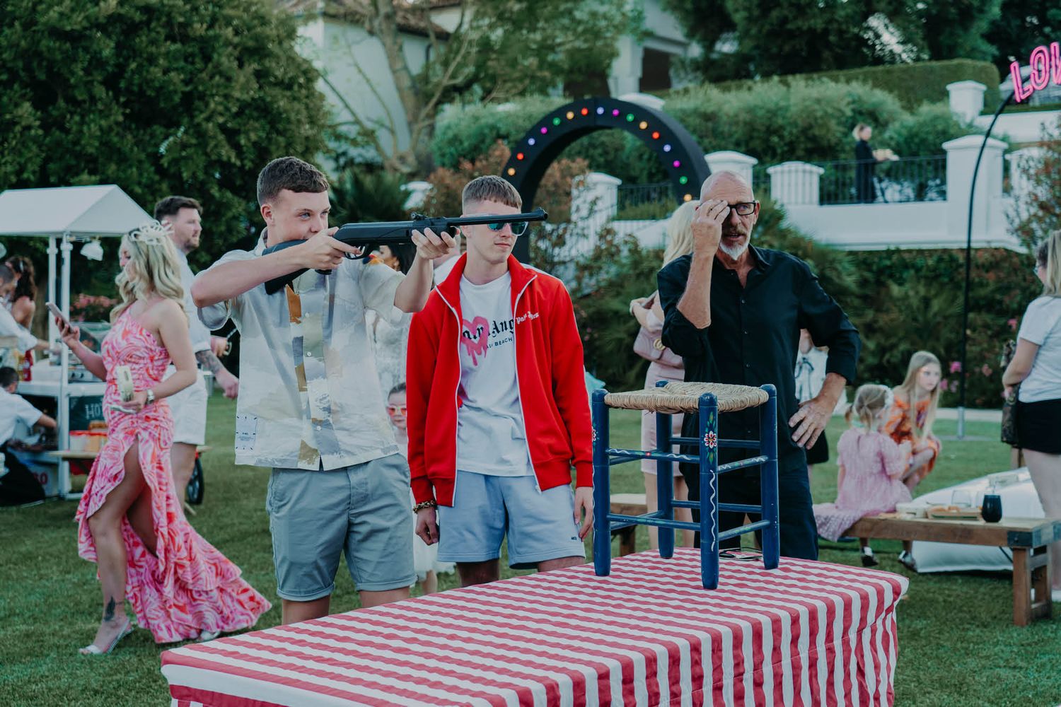 People celebrating at an outdoor party with red and white checkered tablecloth and festive decorations.