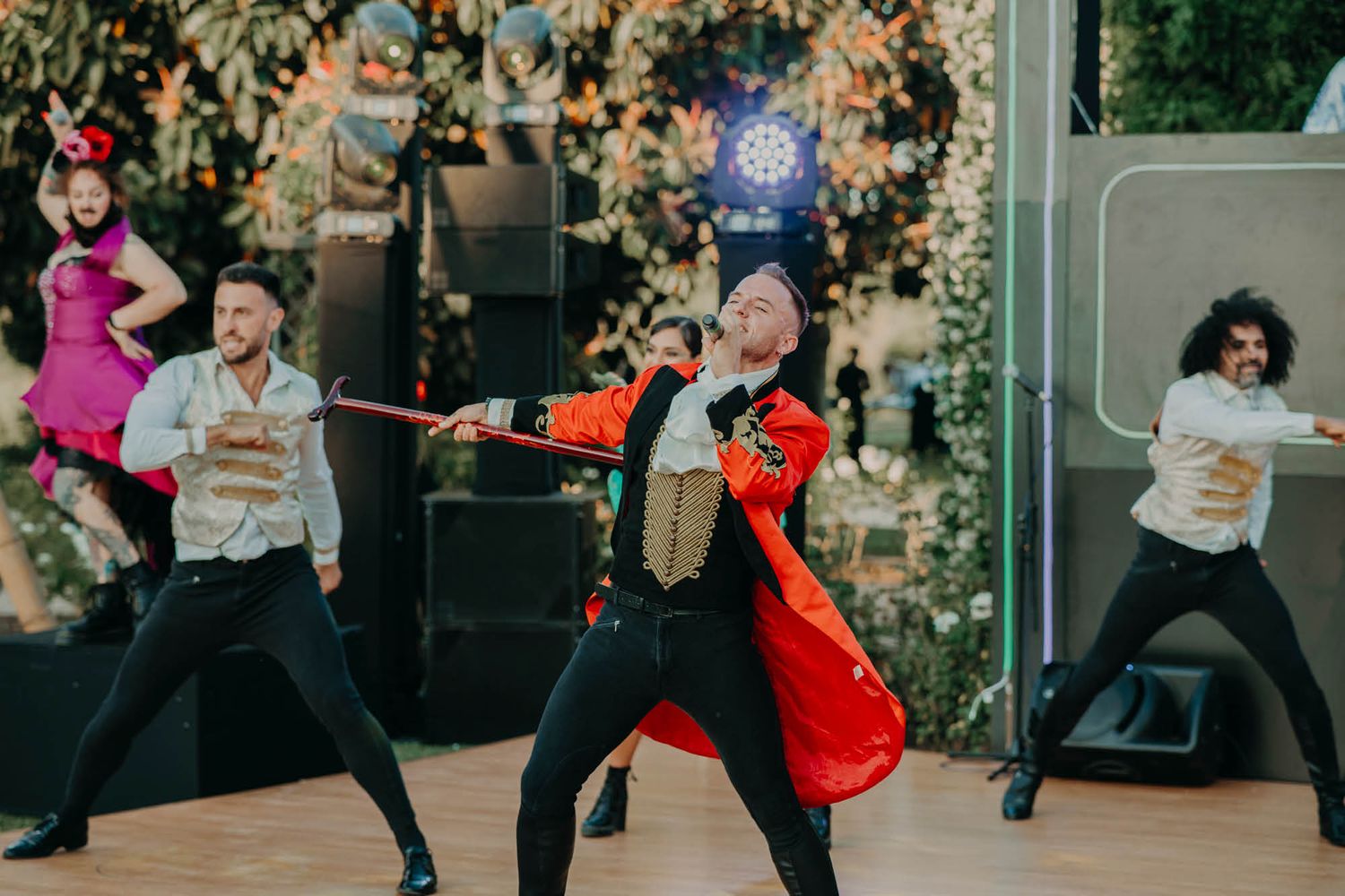 Group of performers dancing energetically in colorful outfits during an outdoor performance with autumn foliage.