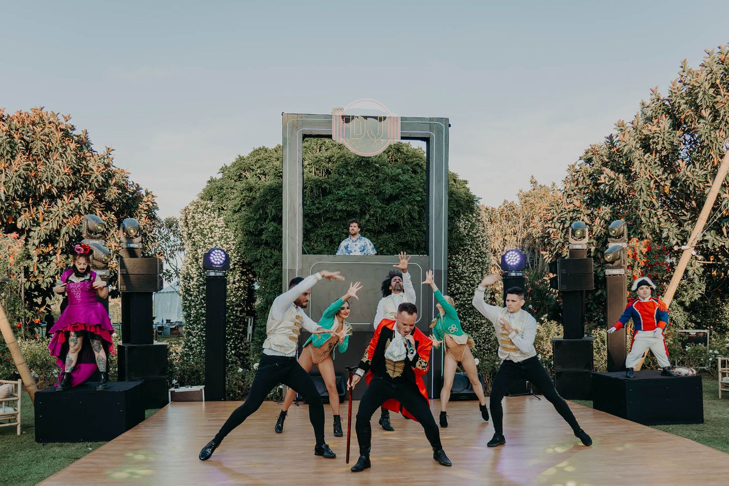 Dancers performing a choreographed routine on an outdoor stage with a metal arch structure backdrop.