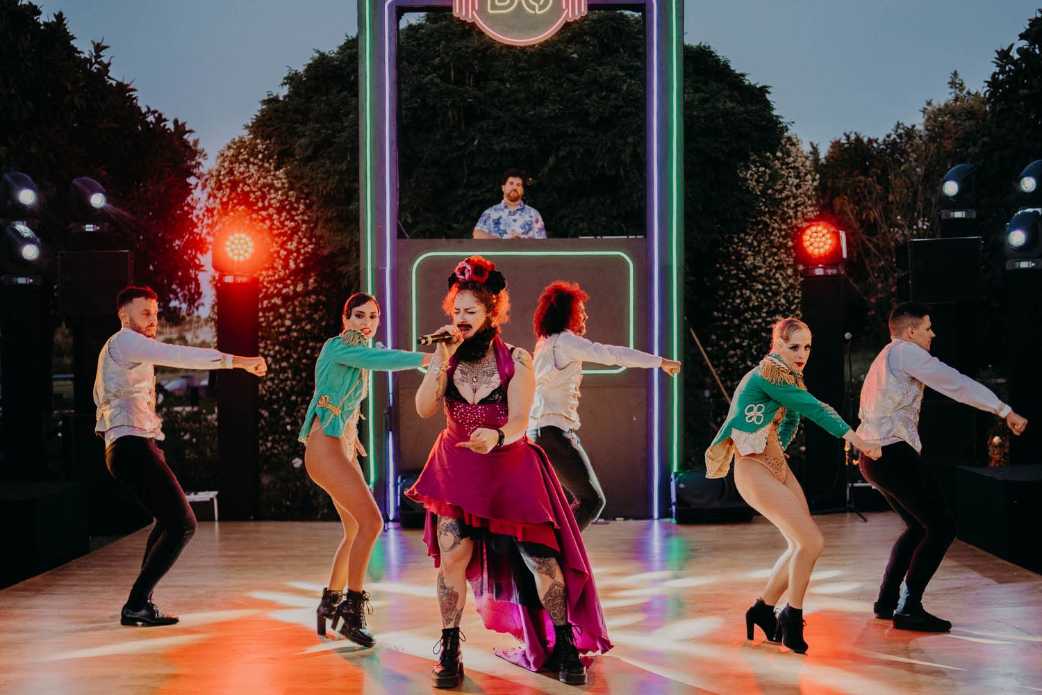Dancers perform an energetic choreographed routine on an illuminated outdoor stage with red lighting effects.