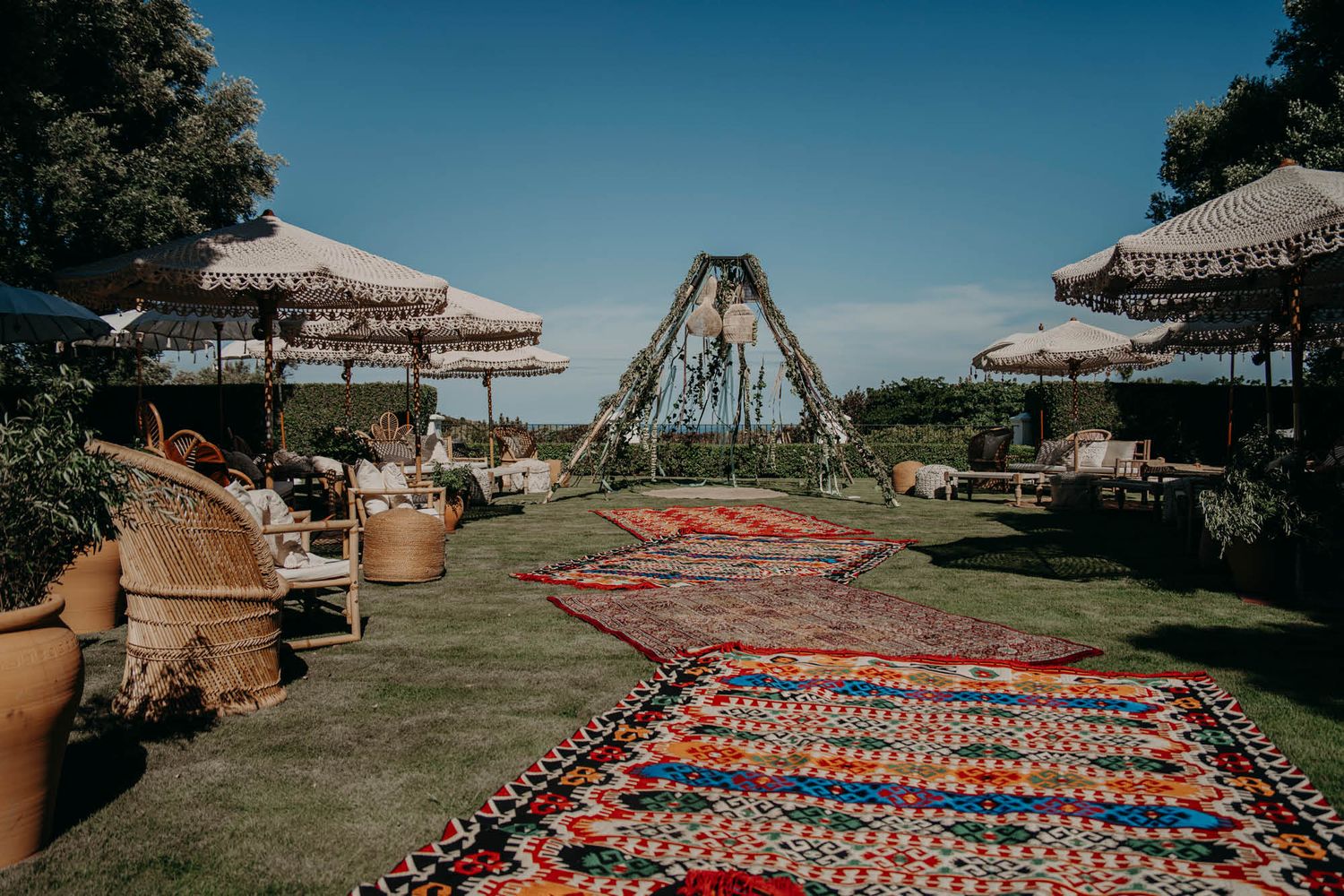 Bohemian wedding setup with colorful rugs and a teepee structure under blue skies.