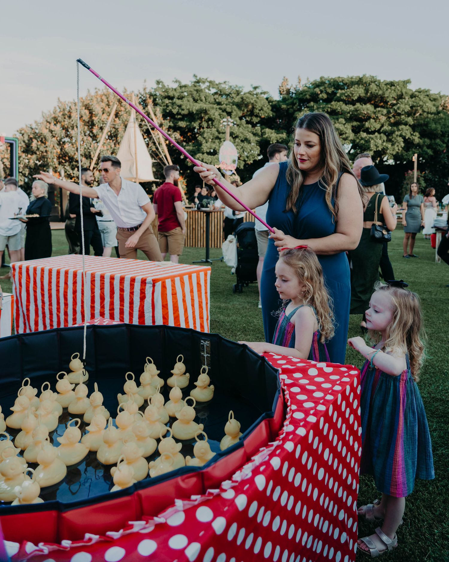 Children playing carnival games at a wedding reception featuring a duck pond with red and white striped decor.