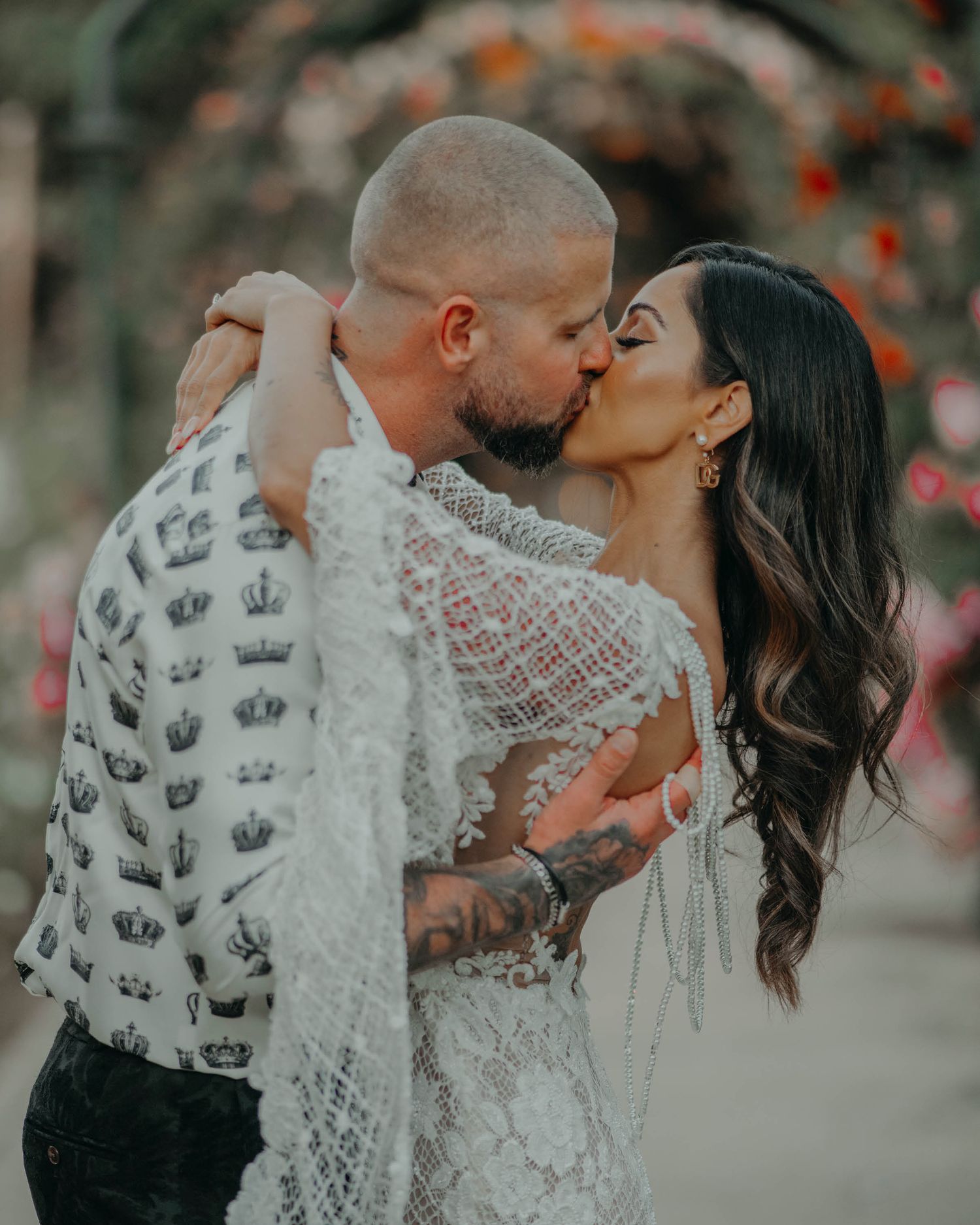 A romantic wedding couple embraces in an intimate moment outdoors with blurred orange flowers in the background.