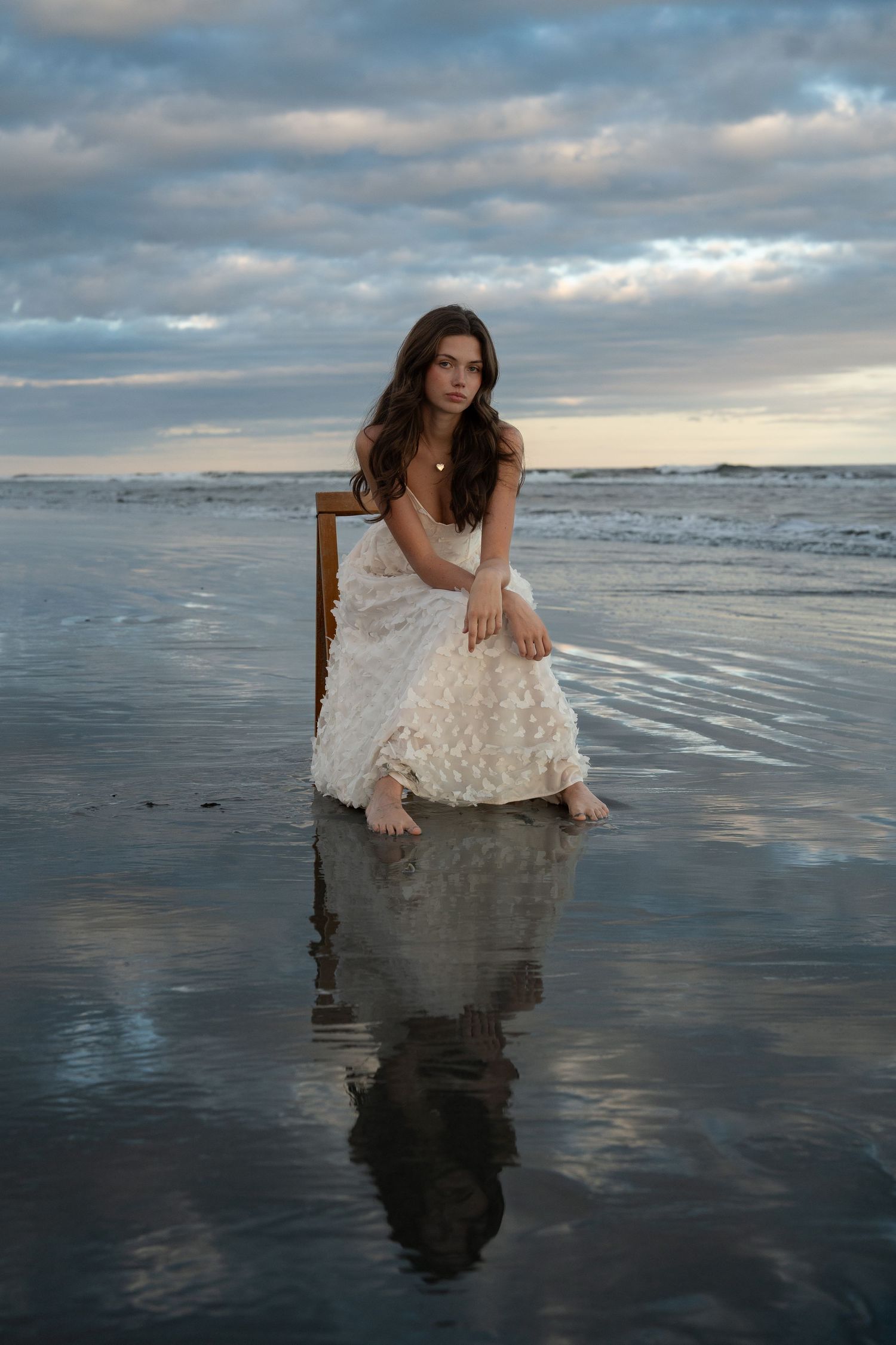 Artistic portrait session on a reflective beach at sunset with a white dress and moody clouds.