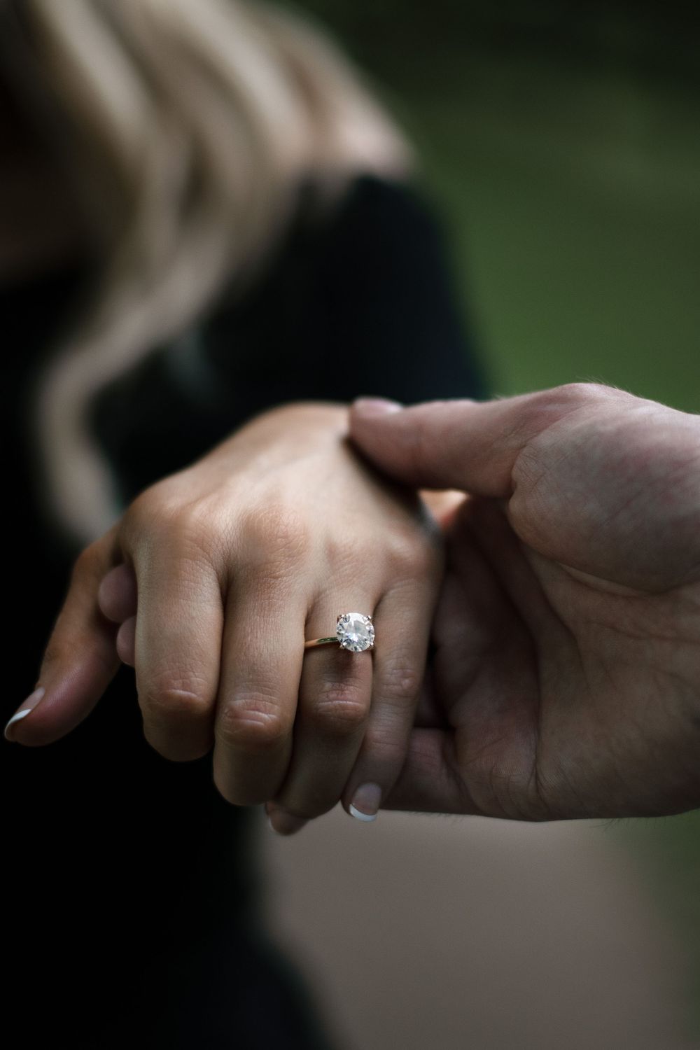 Close-up of hands holding with diamond engagement ring in focus.