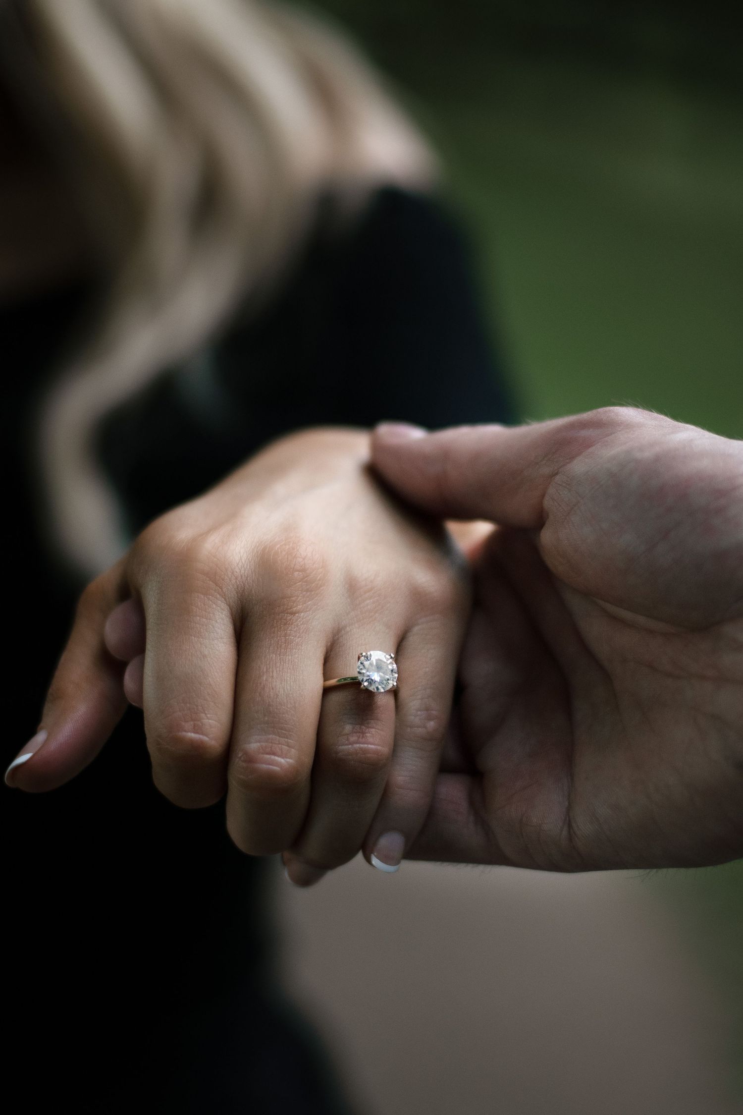 Close-up of hands holding with diamond engagement ring in focus.