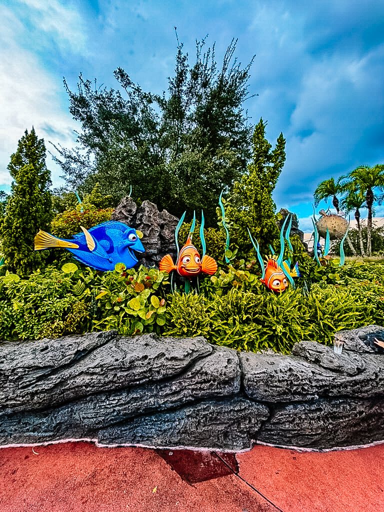 Disney World Finding Nemo themed garden display with colorful fish sculptures among tropical plants against a blue sky.