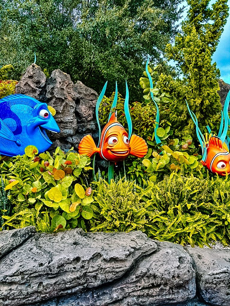 Colorful Finding Nemo-themed garden decorations featuring blue and orange fish characters among rocks and yellow foliage.