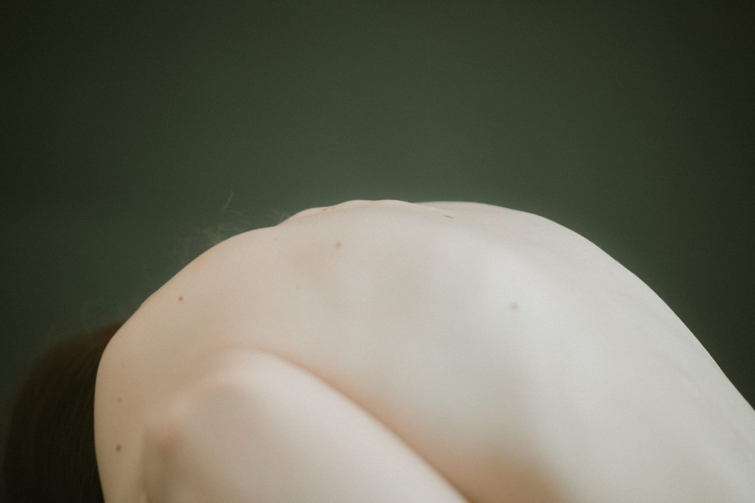 Abstract close-up photo of smooth pale curves against a dark green background.