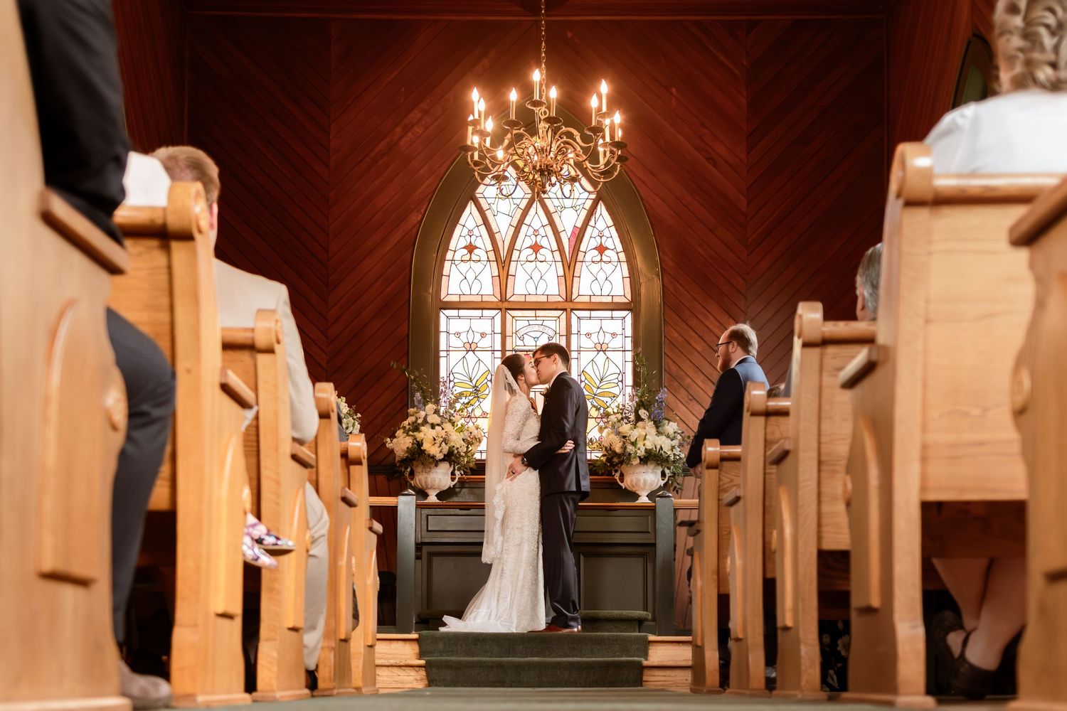 Wedding ceremony in church with stained glass windows and chandelier.