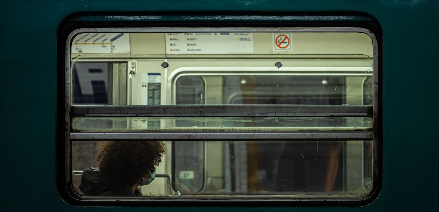 View through a dark train window showing a passenger silhouetted against the interior lighting of a subway car.