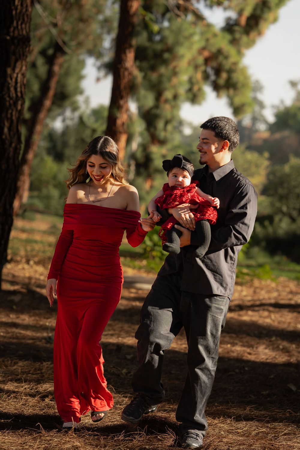 A heartwarming outdoor family photo session in a wooded area with a person in a red dress and two others in gray outfits.