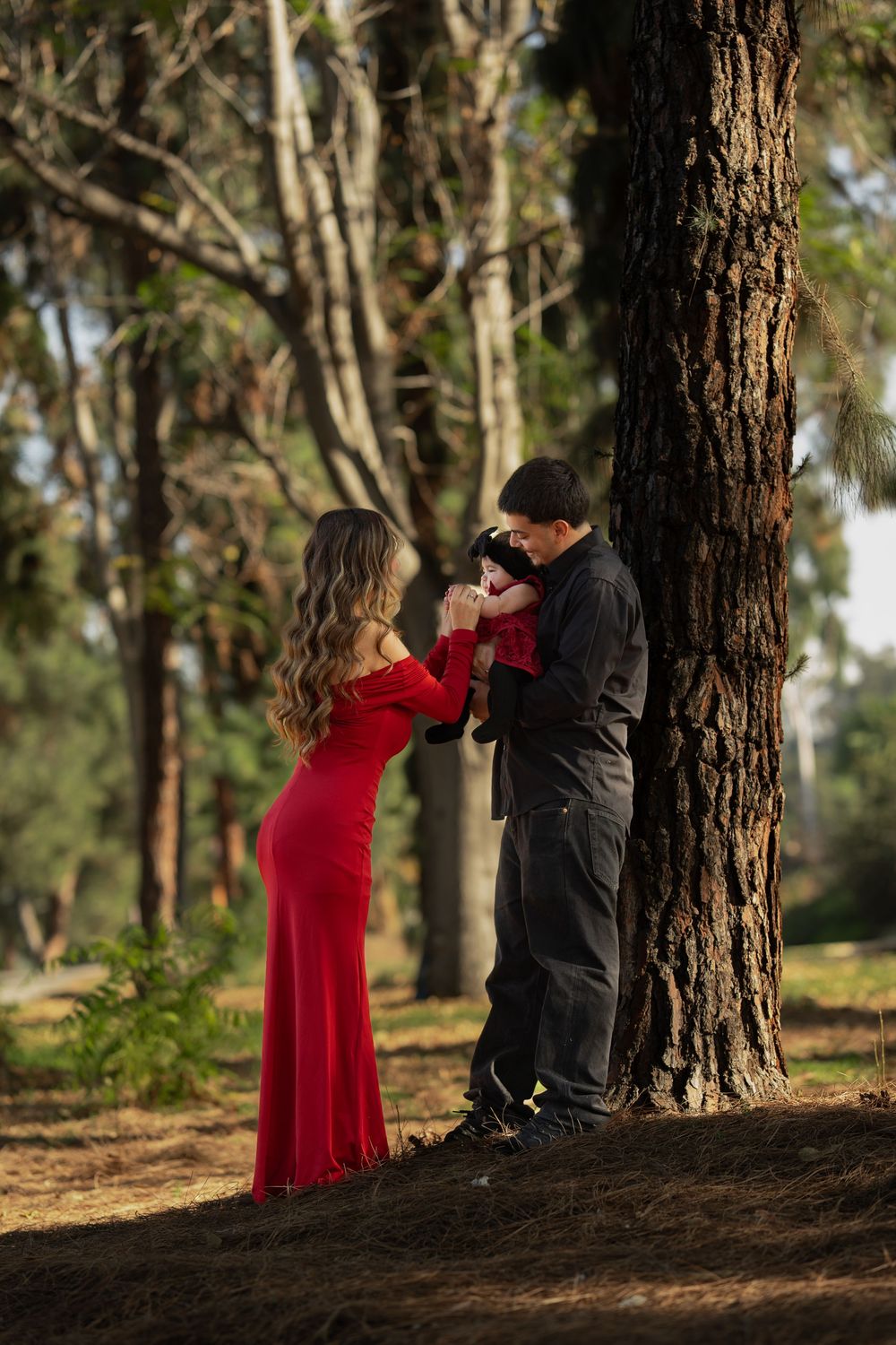 A couple in a forest setting, with one person wearing a flowing red dress and the other in dark clothing by a large tree.