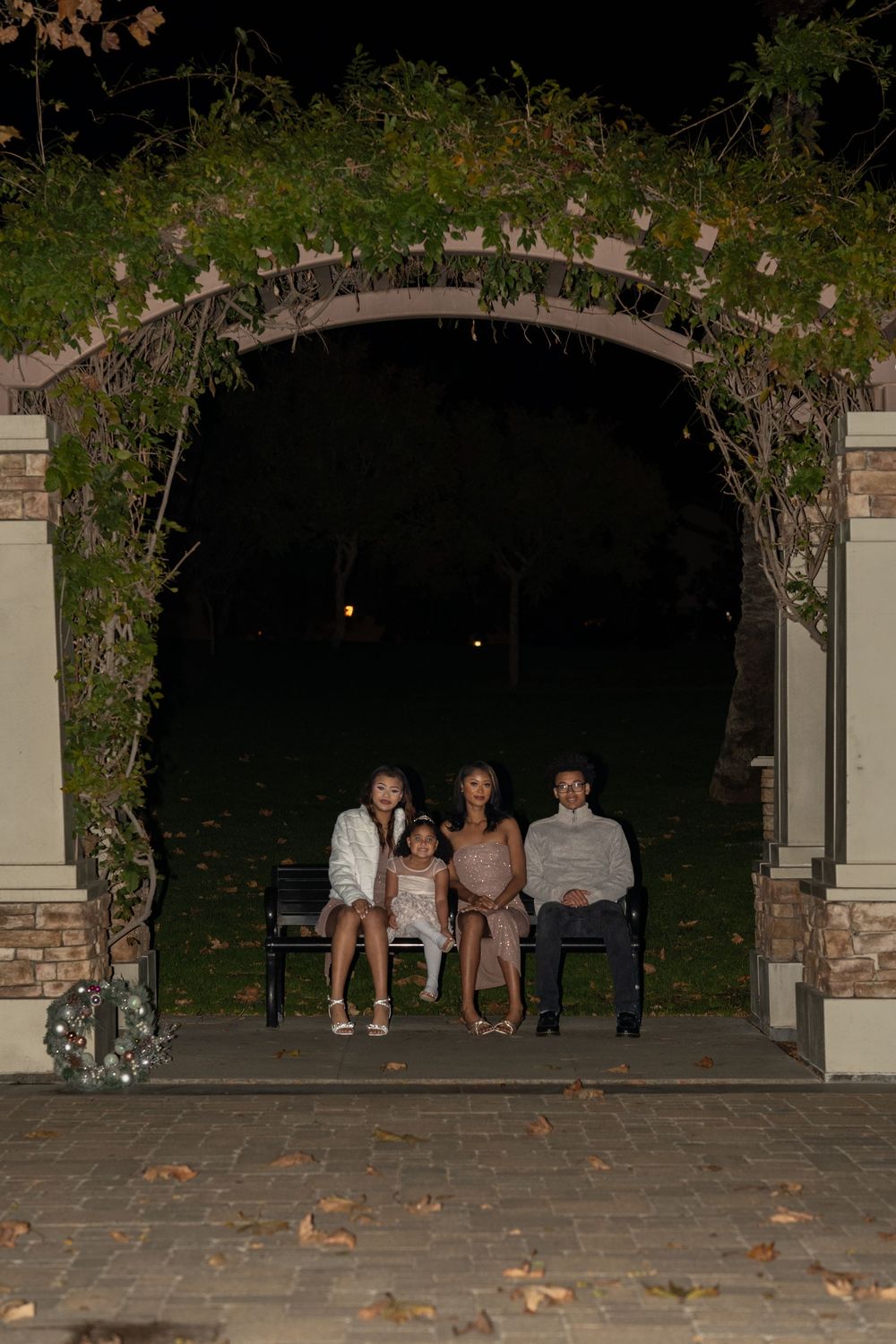 A group of people sitting under an outdoor stone archway at dusk with autumn leaves scattered on the ground.