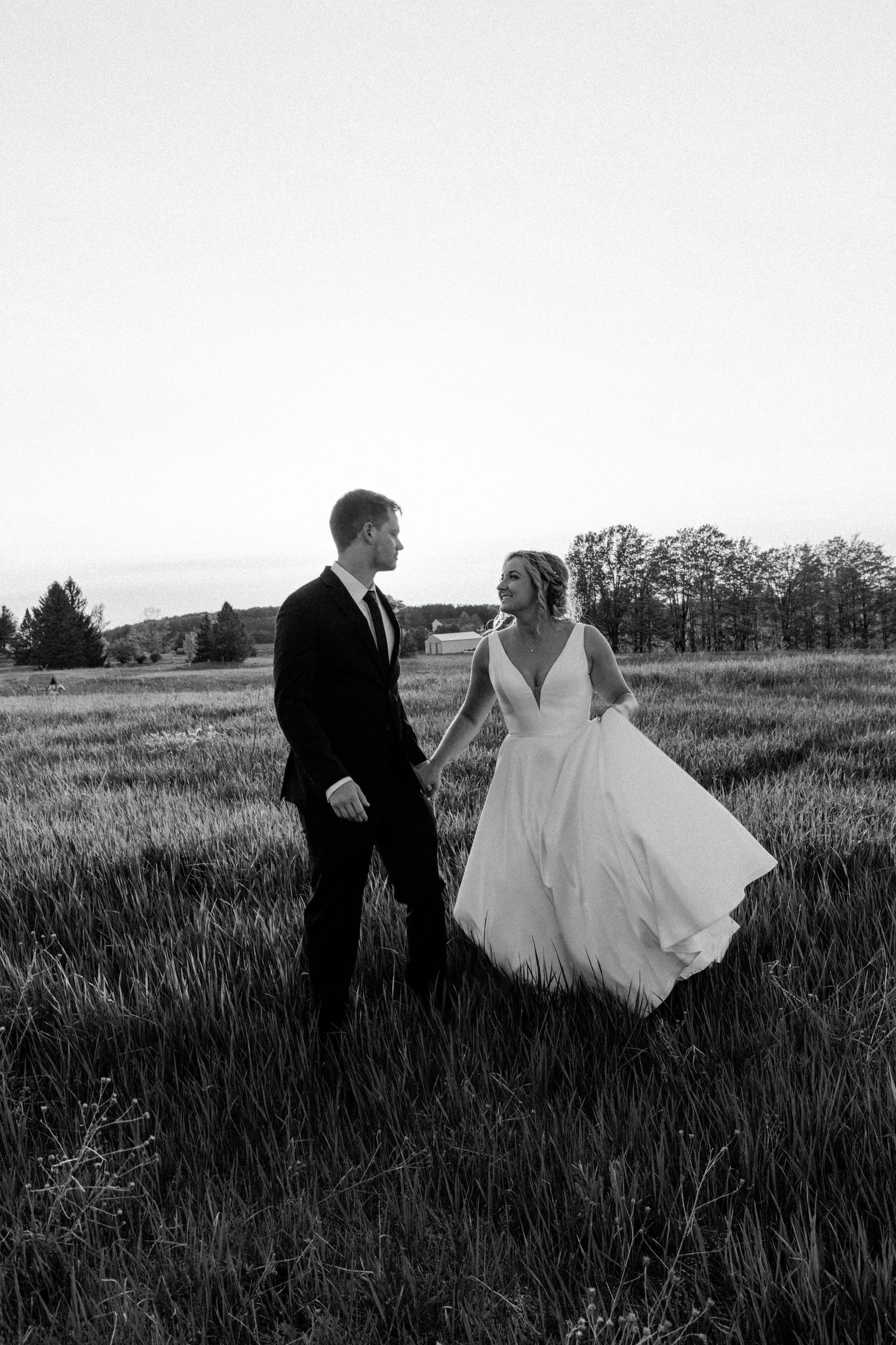 Black and white wedding photo of couple in field with bride's dress flowing in wind.