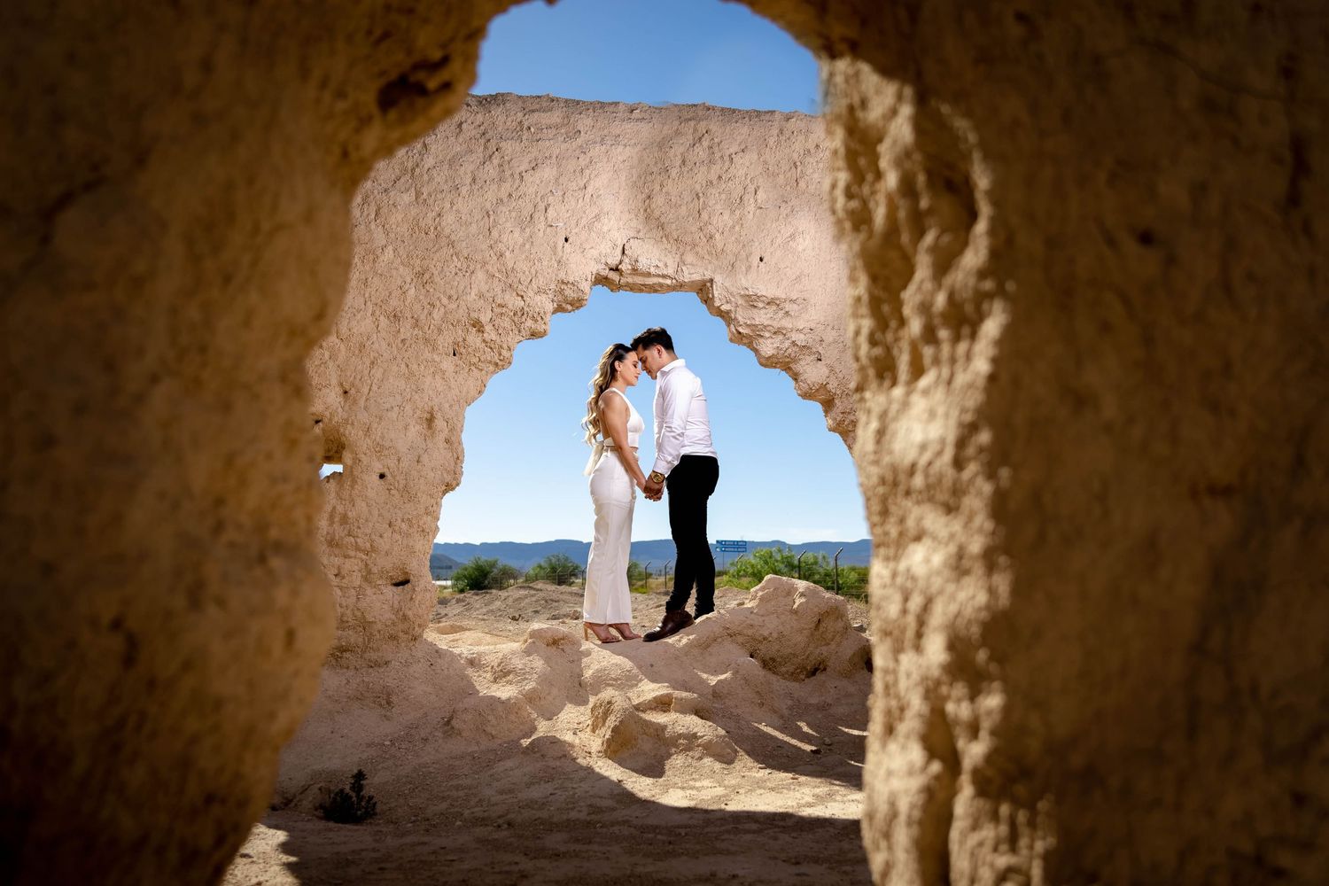 Silhouette of couple framed by natural rock arch formation against desert landscape.