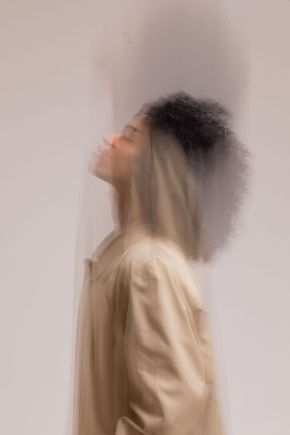 Artistic double exposure portrait showing profile view in cream tones with ethereal motion blur effect.