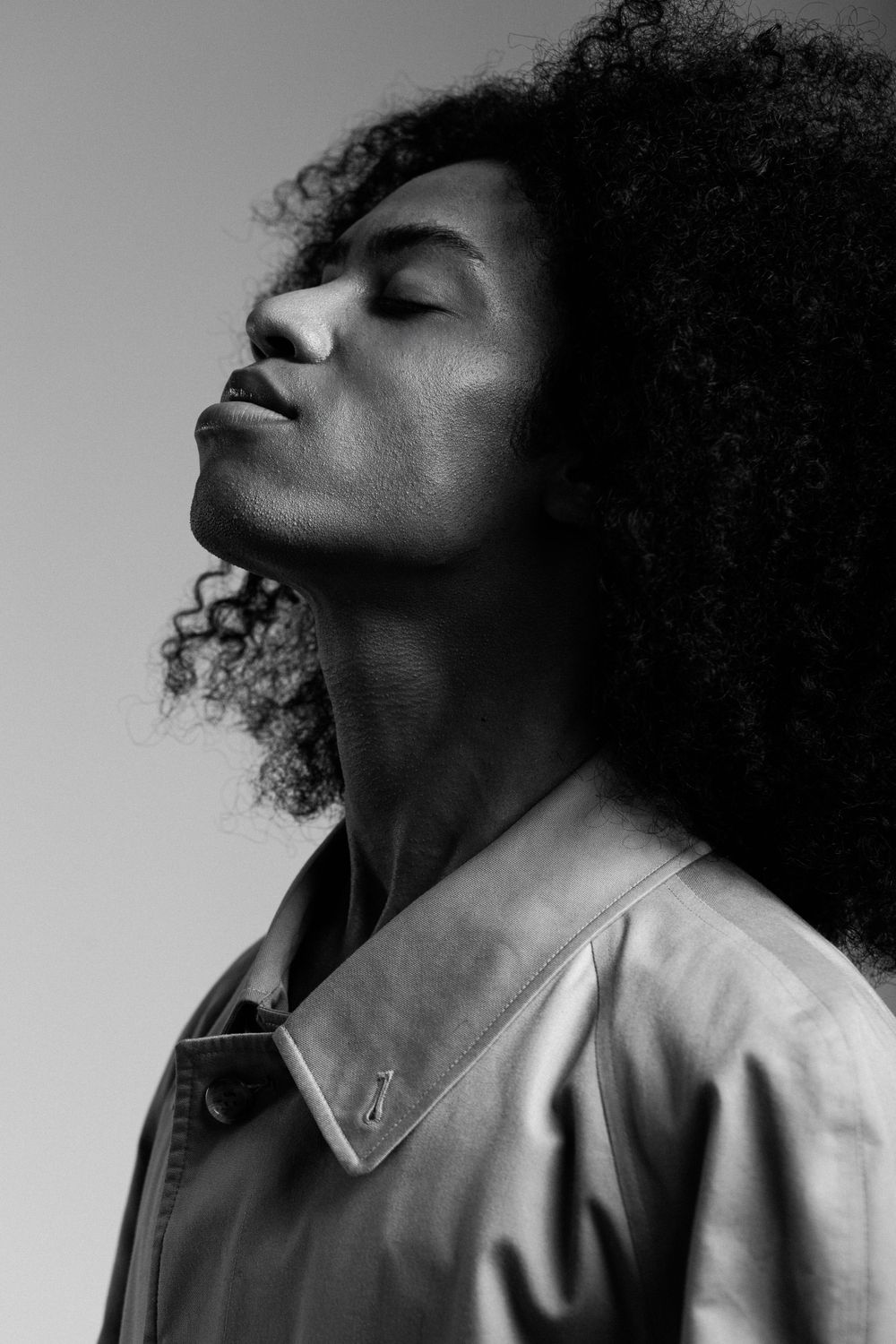 Black and white portrait of person with natural curly hair tilting head back with eyes closed in peaceful expression.