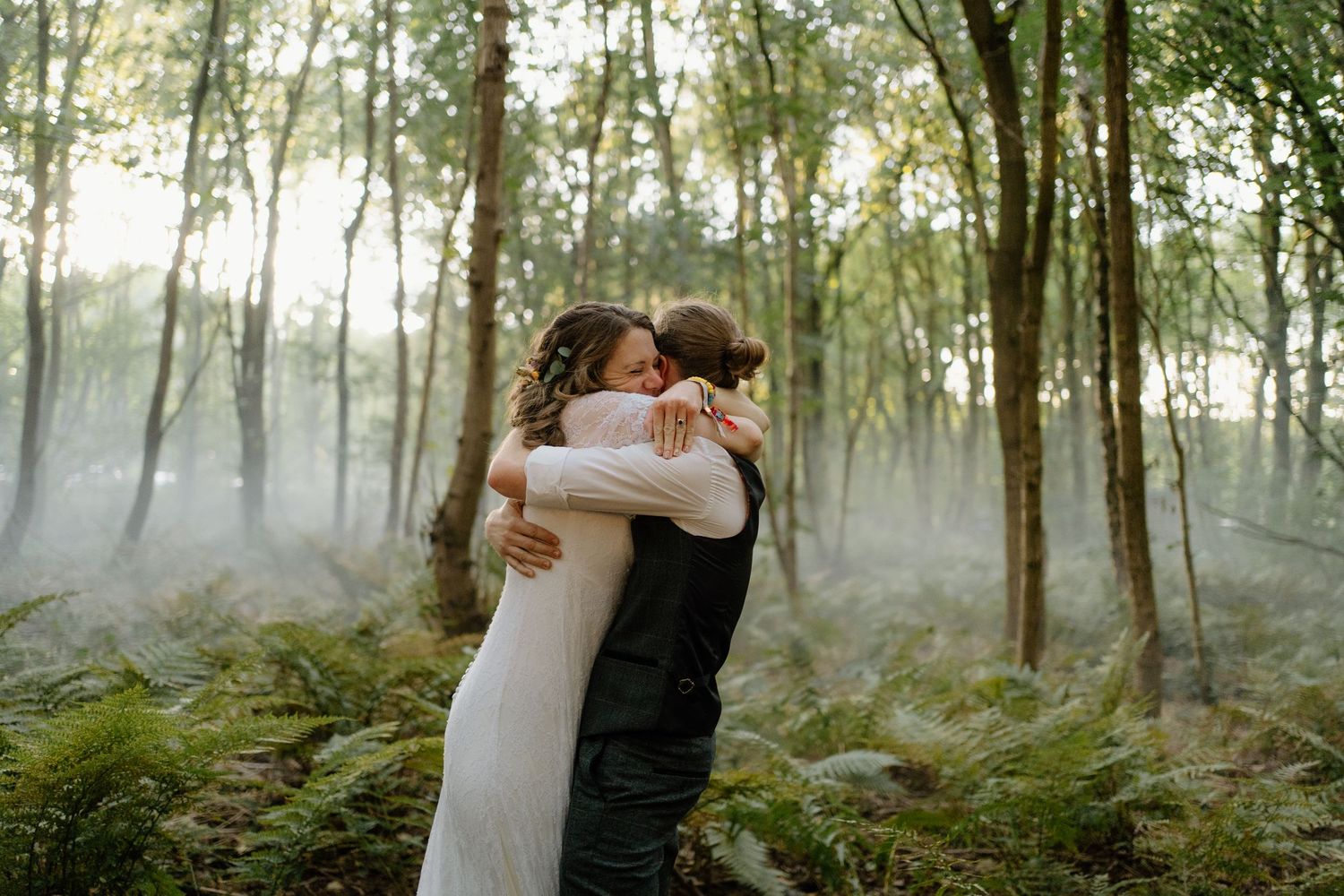 Couple embraces in a misty forest setting wearing wedding attire.