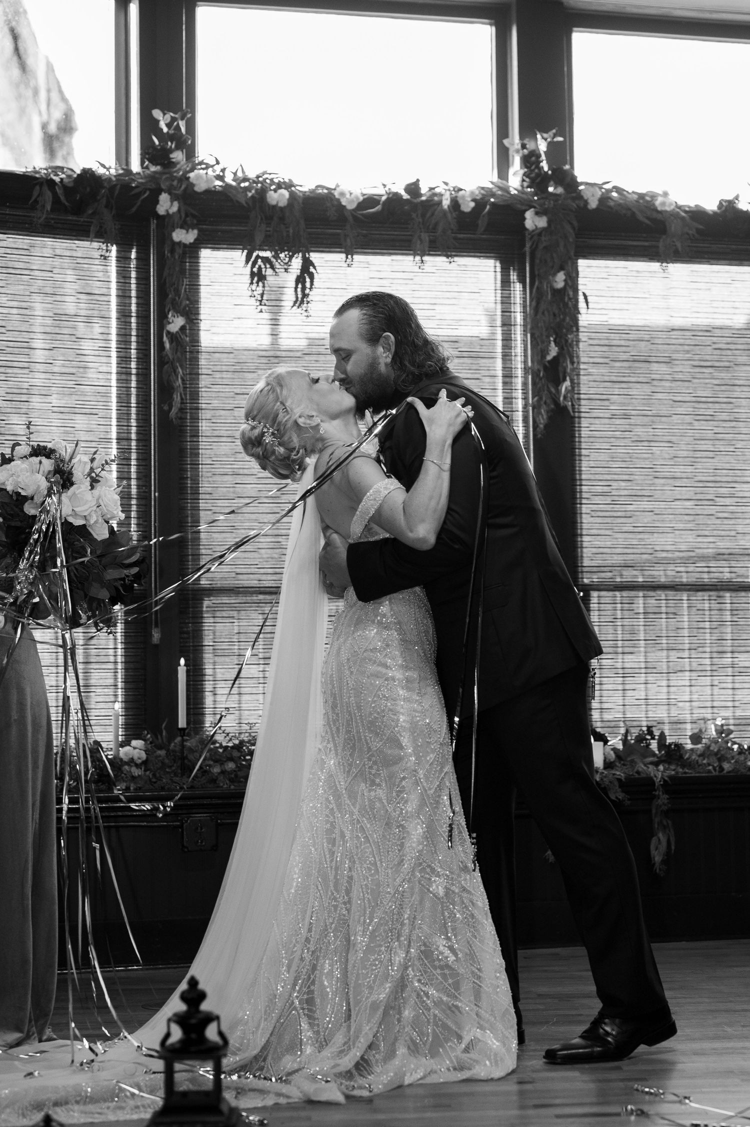 A romantic black and white wedding photo showing a newlywed couple sharing their first dance beneath a floral arch.