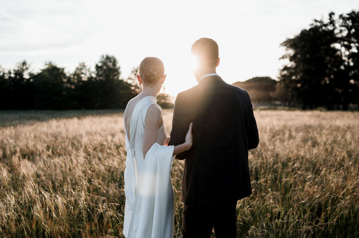 A romantic sunset silhouette of a couple in wedding attire standing in a golden wheat field.