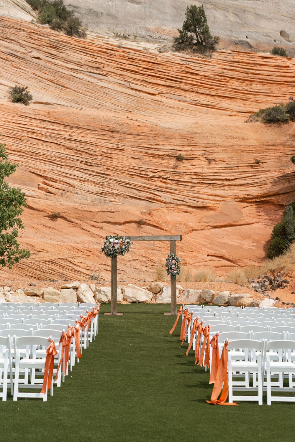 Outdoor wedding ceremony setup with white chairs and orange ribbons against red rock formations.