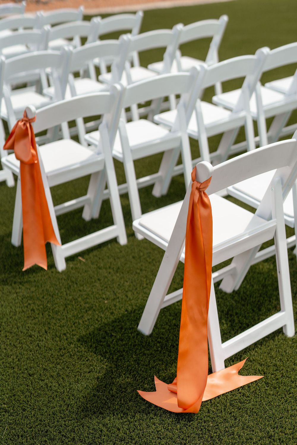 White wedding ceremony chairs with coral ribbons arranged on green lawn.