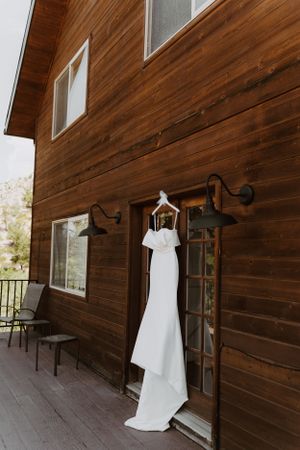 A white wedding dress displayed against rustic wooden walls with outdoor lighting fixtures.