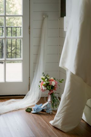 A white wedding dress hanging in a bright room with windows and hardwood floors.