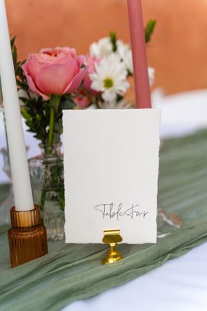 Place cards and candles arranged with pink flowers on a sage green table runner.