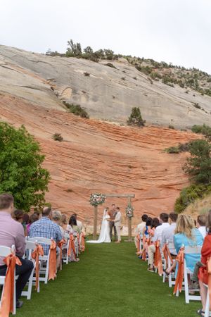 A wedding ceremony setup with white chairs and orange decor against stunning red rock cliffs in a desert landscape.