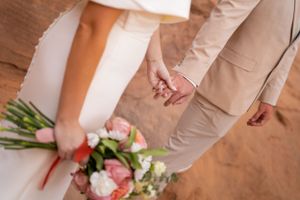 Close-up details of a wedding couple's attire showing tan suit and white dress against red rocks.