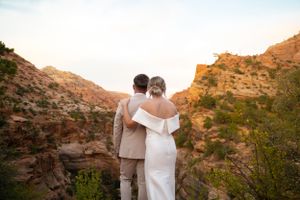 Silhouettes of a wedding couple against the warm glow of desert cliffs at sunset.