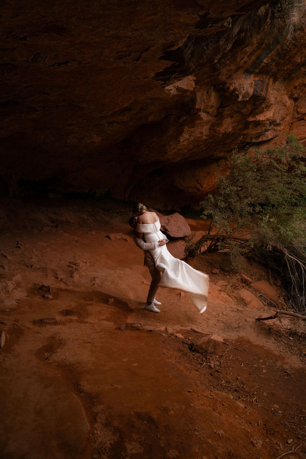 A dramatic wedding photo shoot in a dimly lit desert cave with red rock walls.