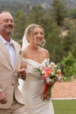Joyful wedding couple shares a laugh while holding a coral and white bouquet outdoors.