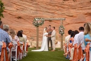 Outdoor wedding ceremony with wooden arch and red rock formations in the background.