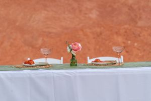Romantic table setting with wine glasses, plates and a pink rose centerpiece on a white tablecloth.