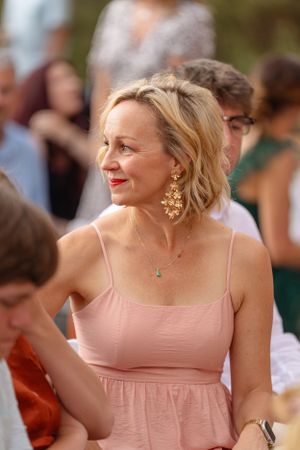 Wedding guest in a blush pink dress smiles during an outdoor celebration.