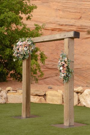 Wooden posts decorated with floral arrangements line a grassy outdoor wedding ceremony space.