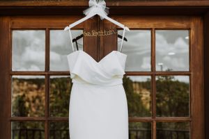 Elegant white wedding dress on personalized hanger displayed against wooden door panels.