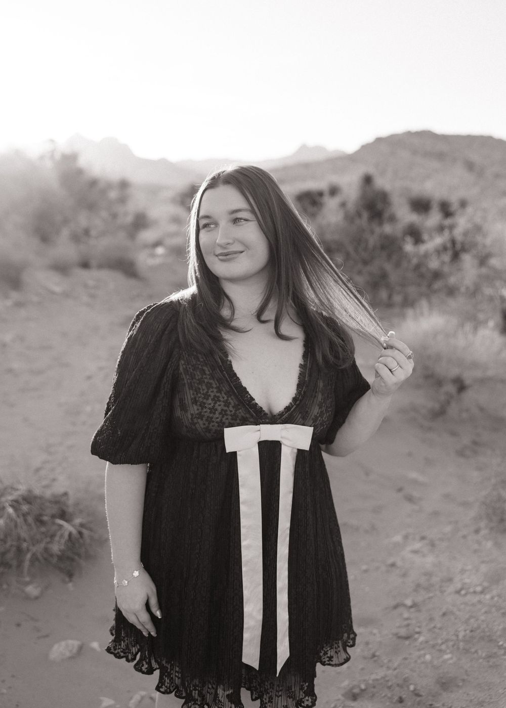 Black and white portrait of someone in a vintage-style dress with lace details against a desert landscape.