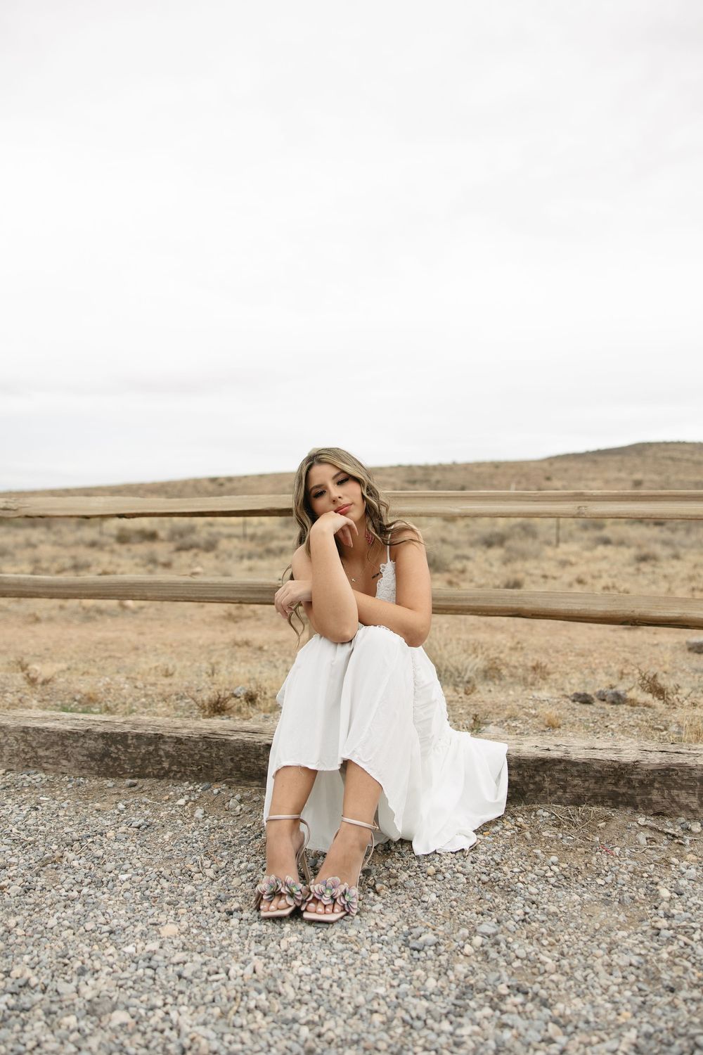 Young woman in white dress sitting on rocky desert terrain during a golden hour photoshoot.