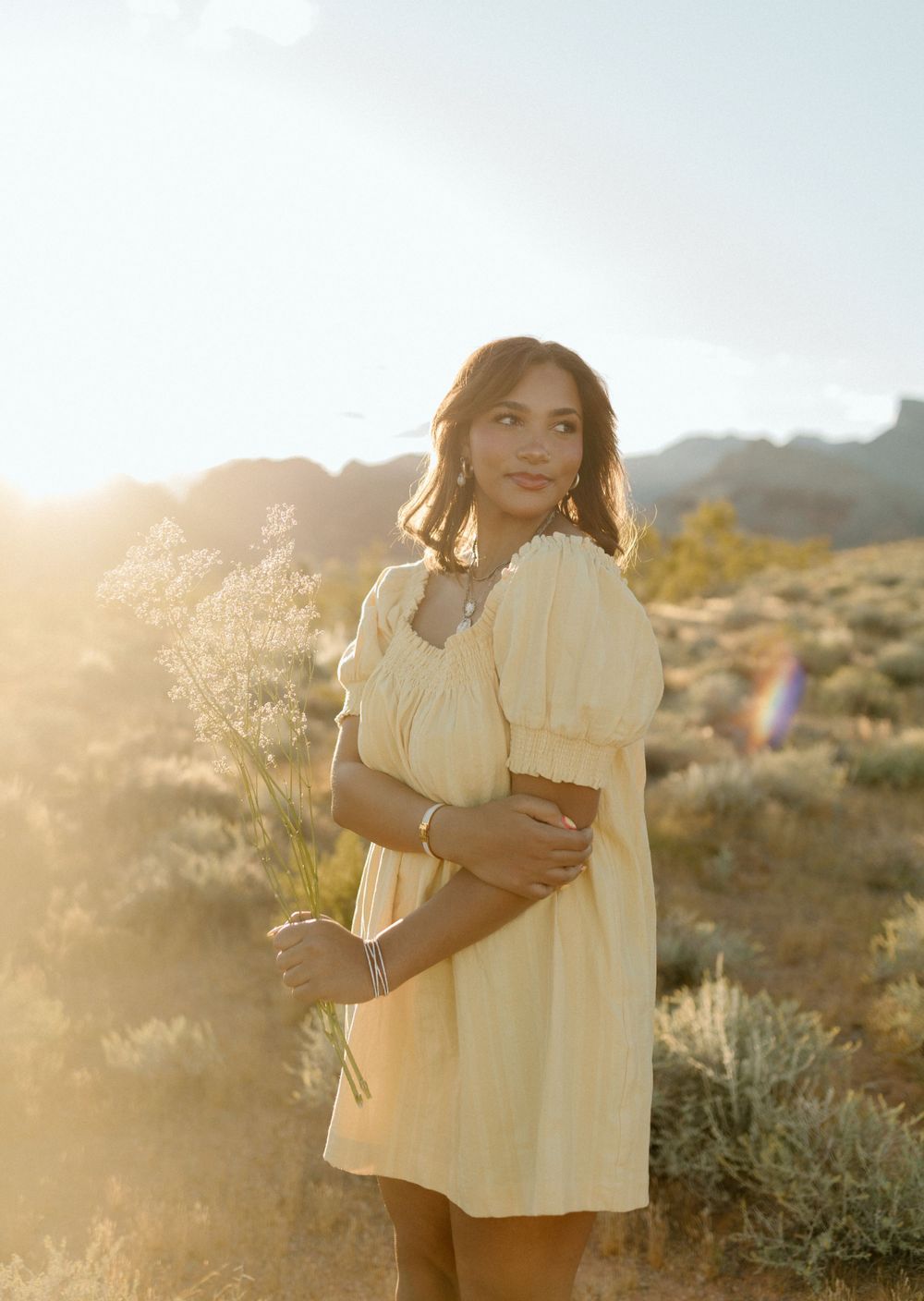 Person in yellow dress holds dried flowers during golden hour in desert setting.