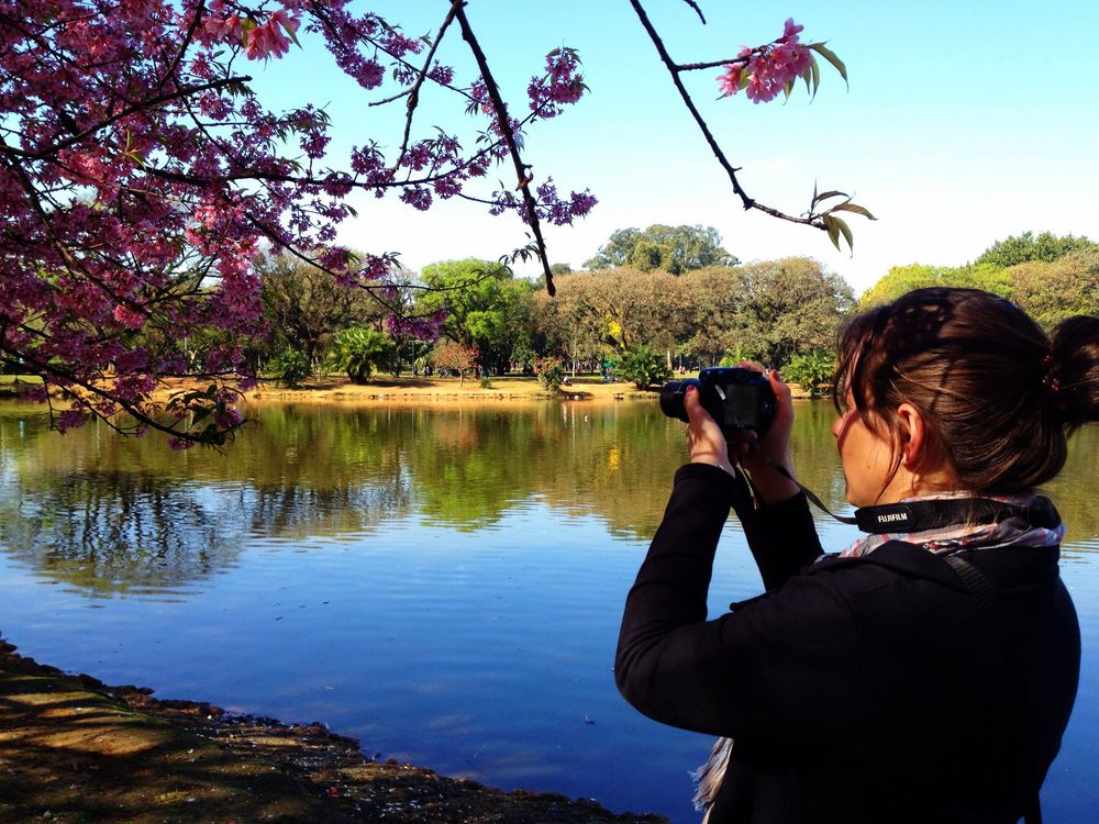 Photographer captures scenic lake view with red autumn foliage framing tranquil water reflection on sunny day.