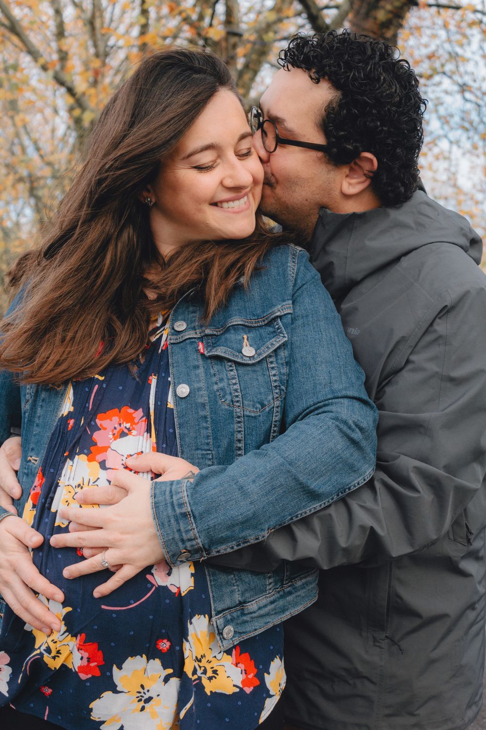 A couple shares an intimate moment outdoors in autumn, with the woman wearing a floral dress and denim jacket.