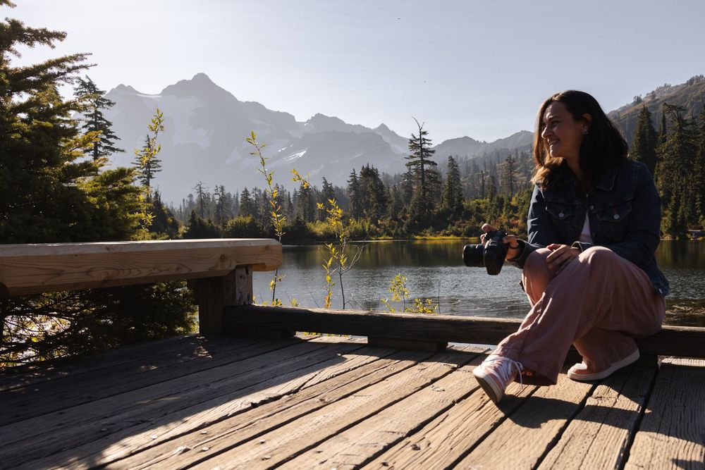 A scenic mountain lake view with wooden deck railing and evergreen trees in the background during golden hour.