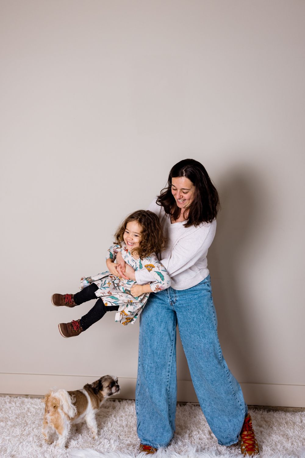 A sequence of playful interactions between a person in blue jeans and a small dog against a white wall.