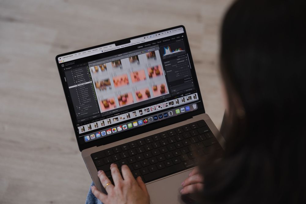 Person editing photos on multiple laptop screens showing a digital photography workflow in dark lighting.
