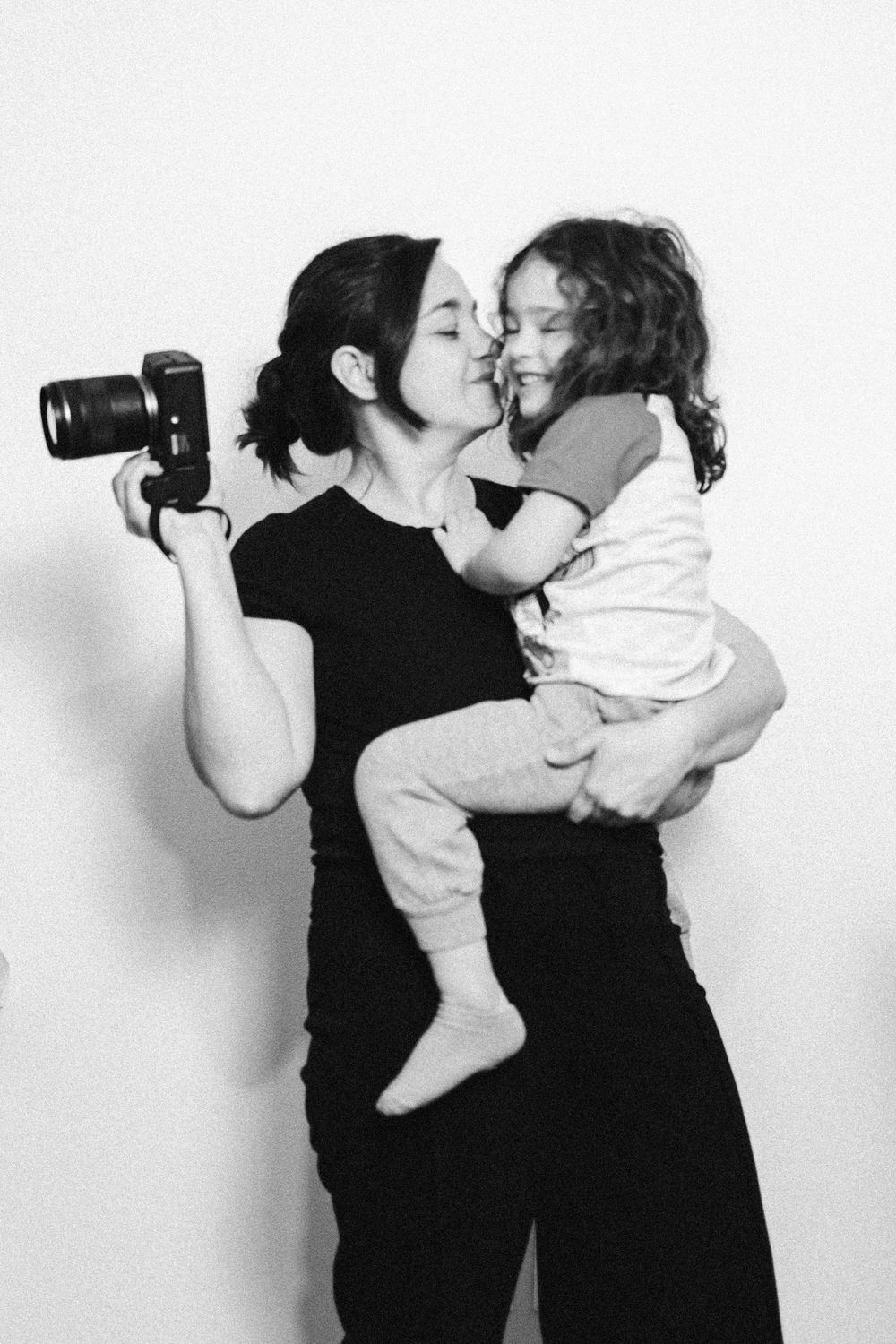 A series of four black and white photos showing a parent holding a baby while taking photos with a camera.